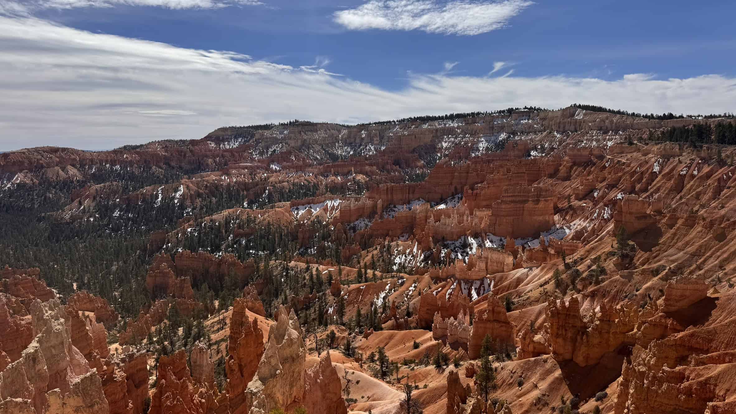 A striking panorama of the orange hoodoos of Bryce Canyon under a stormy sky alongside a bright rainbow and rain curtains