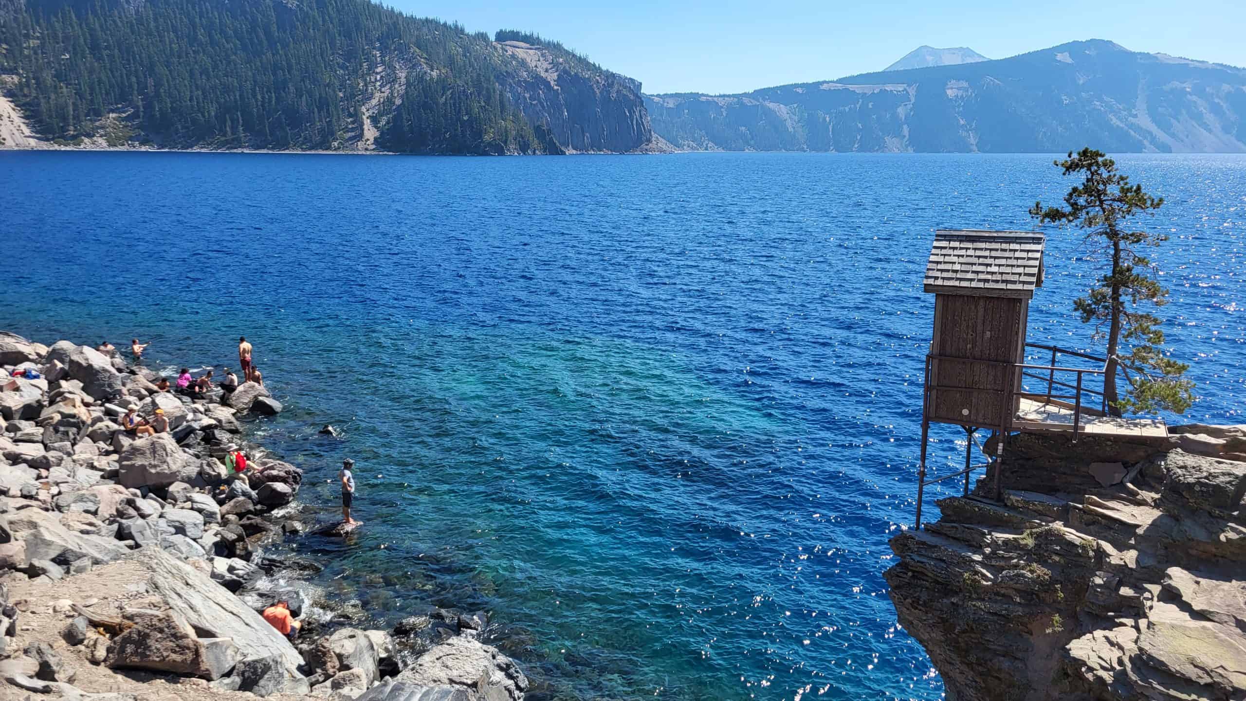 A wooden platform and rocky shoreline overlooking the deep blue water of Crater Lake at Cleetwood Cove."
