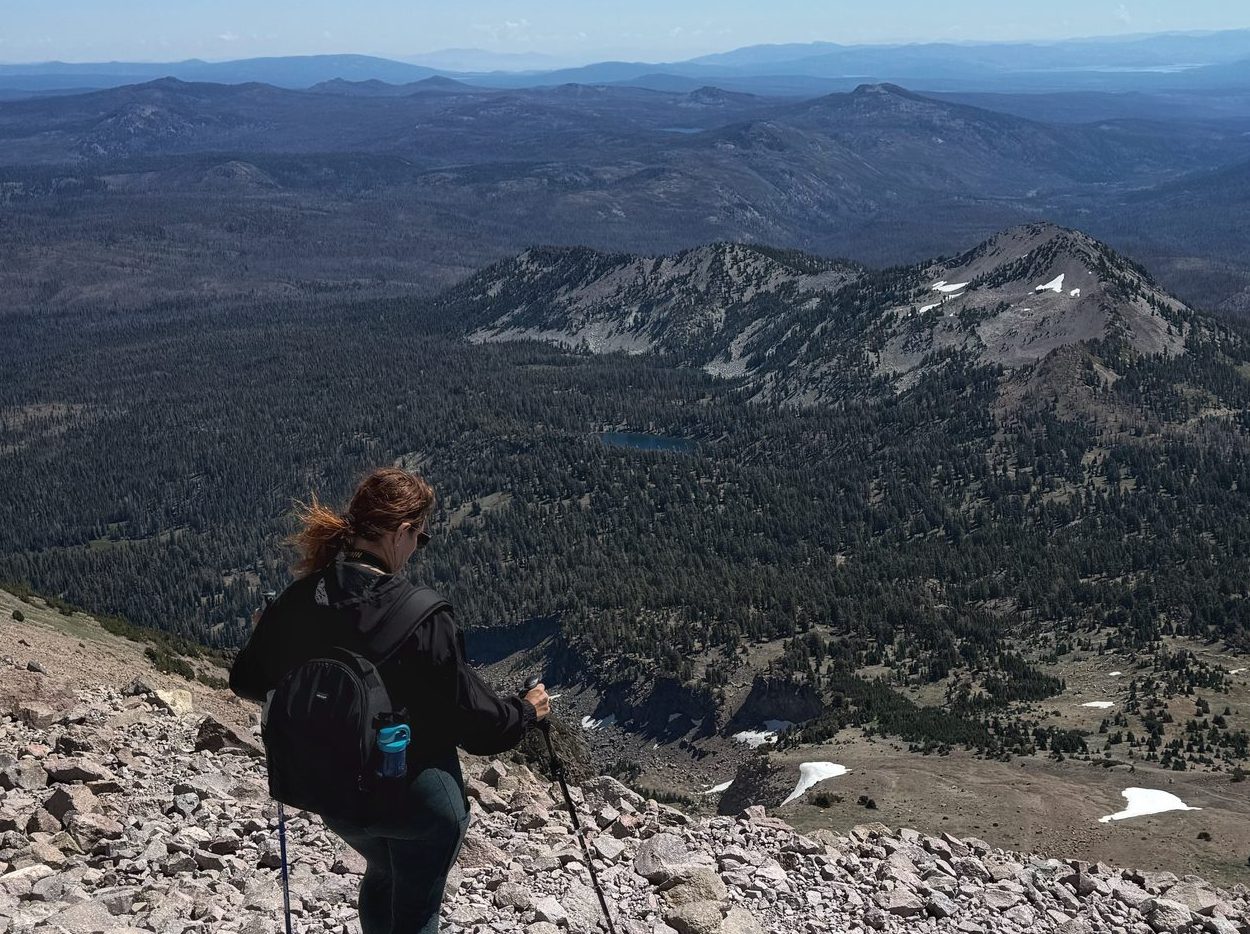 Hiker making her way down the Lassen Peak trail with the distant volcanic landscape fading into distant mountain ridges.