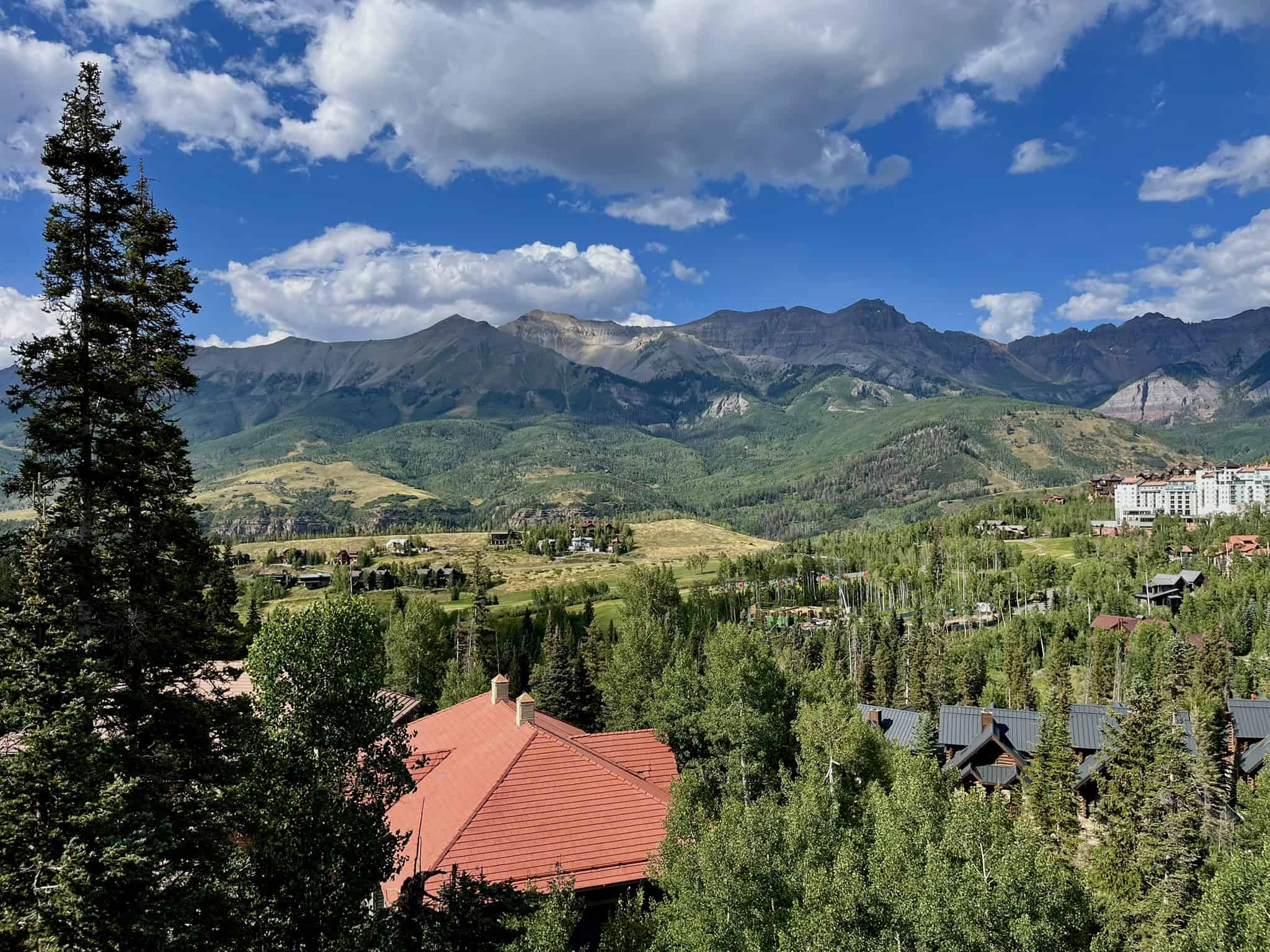 A red-roofed building overlooks a lush valley and rocky peaks, showcasing the spectacular scenery found on popular telluride hikes.

