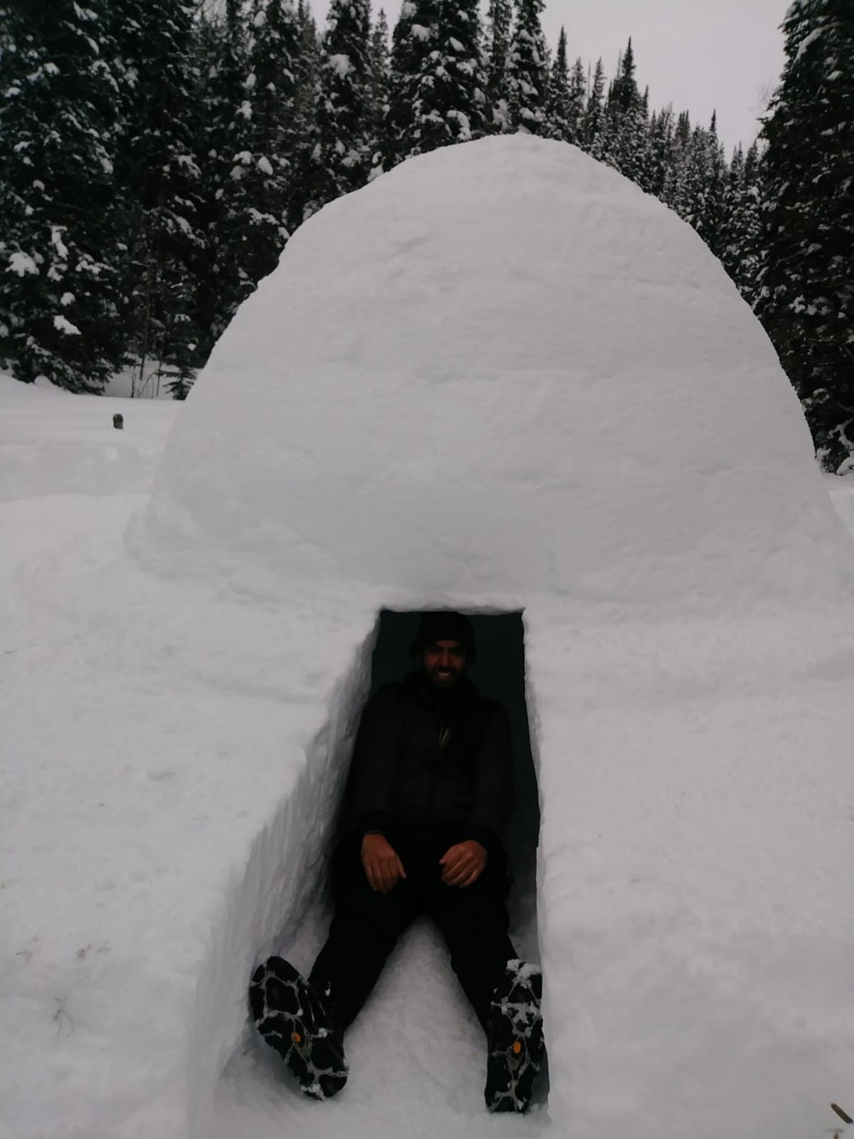 Snow shelter built near Donut Falls, with a hiker seated inside the entrance after a winter snowfall.