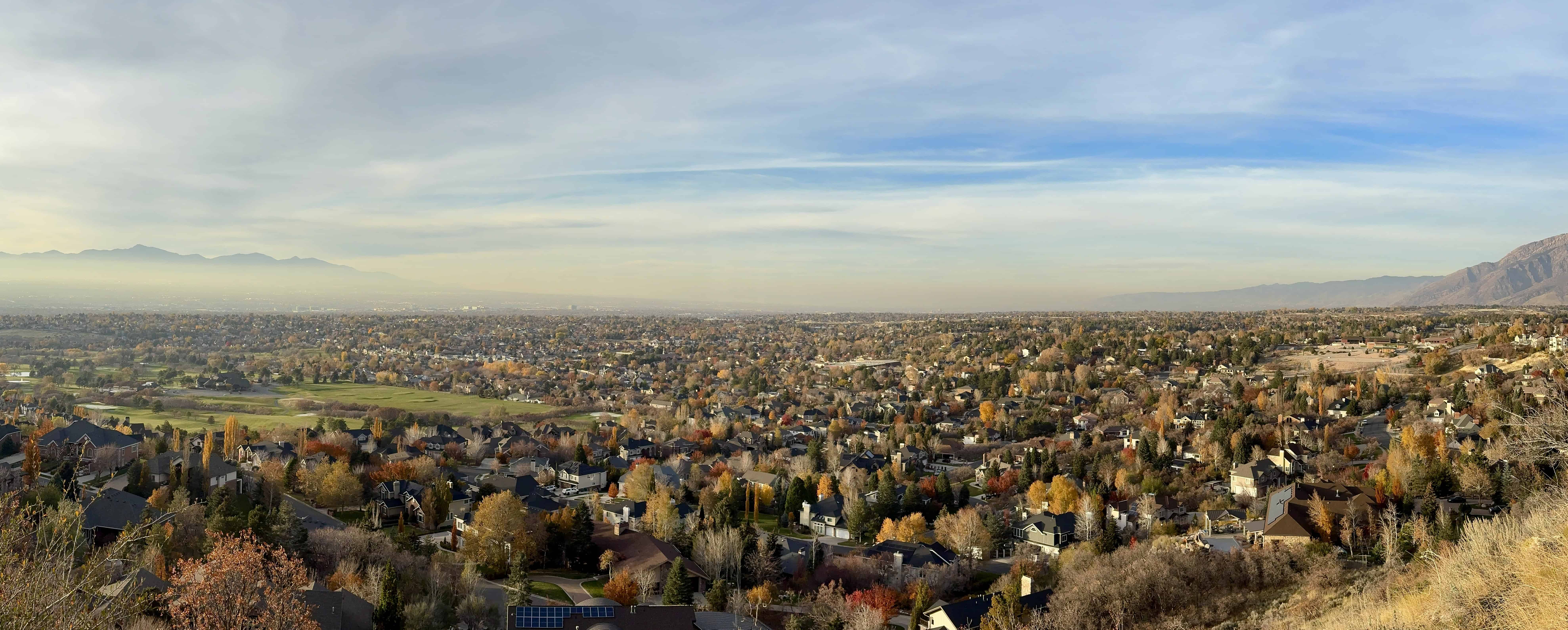 A panoramic view of a city with autumn-colored trees and mountains in the distance, a classic view from the Bonneville Shoreline Trail