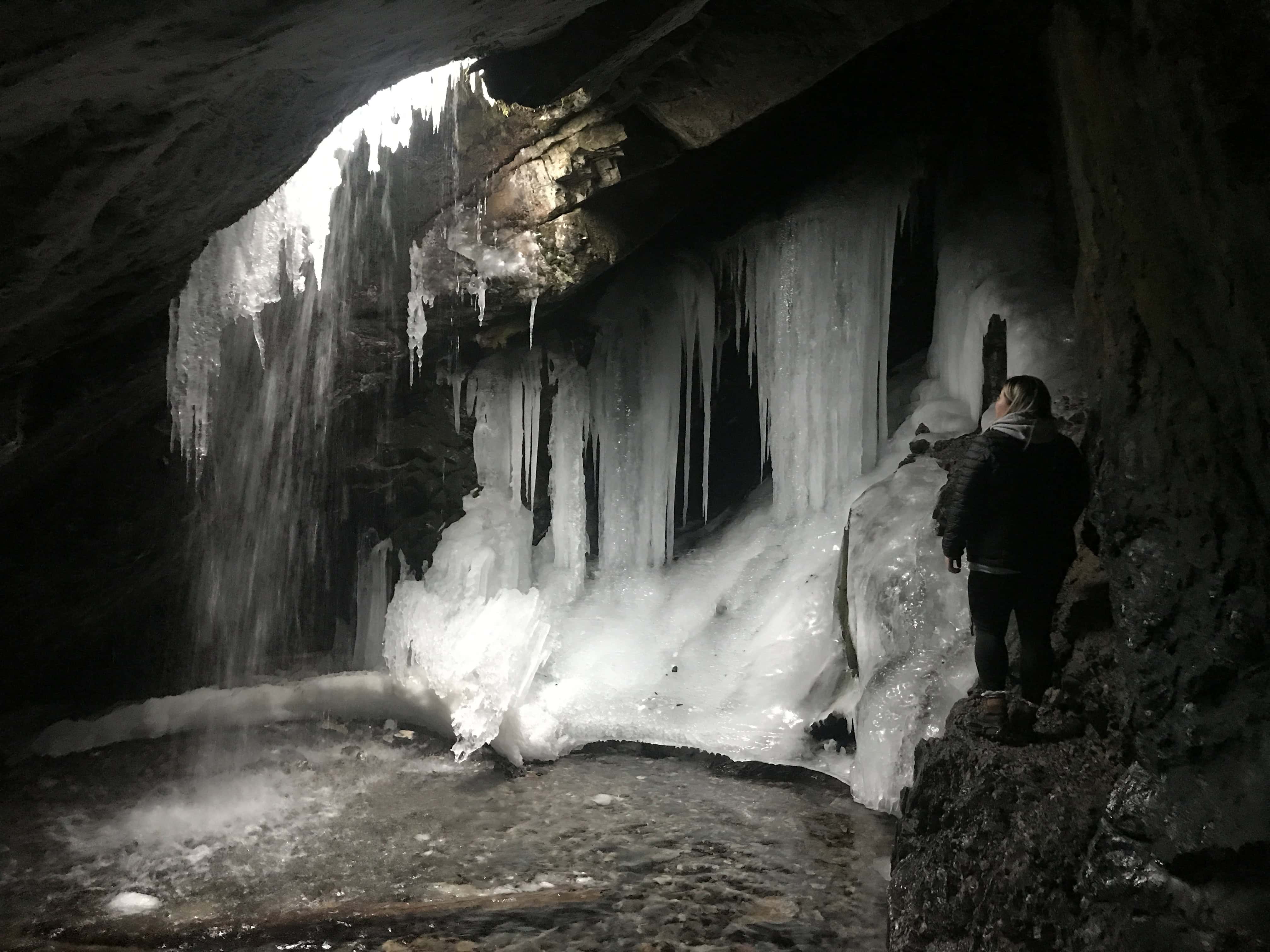 Partially frozen Donut Falls cascading through its famous rock grotto, surrounded by large icicles in winter.