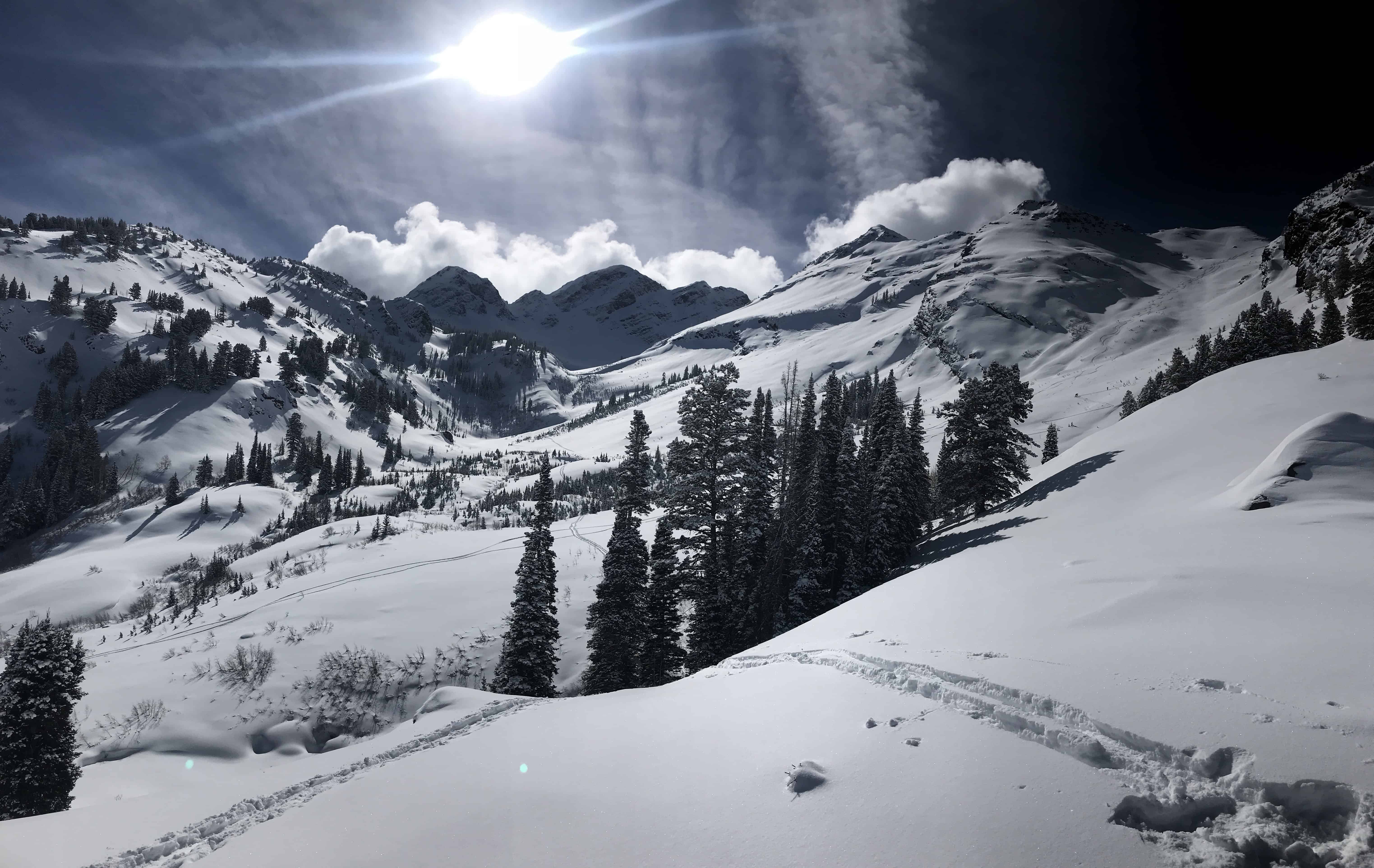 A vast, snow-covered mountain valley with tracks in the snow, illustrating heavy snowpack conditionss